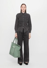 Camisa de ganga cinza com fecho de botão e bolso, combinada com calças largas de corte igual. Uma bolsa tote verde-claro com alças é segurada numa mão.