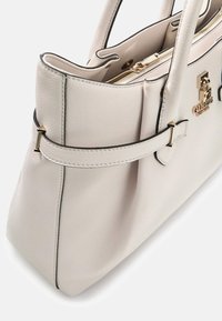 Jasnobeżowa skórzana torba na ramię ze złotymi okuciami, z zamkiem błyskawicznym i dekoracyjnym paskiem. Teksturowana powierzchnia z kontrastującymi czarnymi akcentami.
