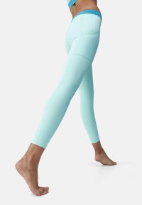 Leggings acquamarina con una vita alta, caratterizzati da una texture liscia e un design aderente, che evidenzia le cuciture e una fascia in contrasto di colore.