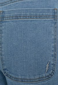 Plave traperice s stražnjim džepom sa vezom munje, istaknutim šavovima i mekanom teksturom. Klasični dizajn s pet džepova.