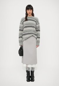 Sivi prugasti džemper širokog kroja, upareni sa sivom suknjom slojevitom preko bijele čipkaste obrube. Crne kožne čizme do koljena i crna torba.