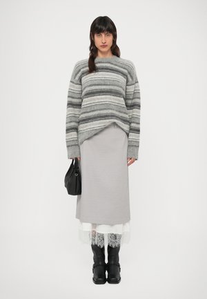 Szary sweter w paski o luźnym kroju, zestawiony z szarą spódnicą z warstwą białej koronkowej lamówki. Czarnie skórzane wysokie kozaki i czarna torebka.