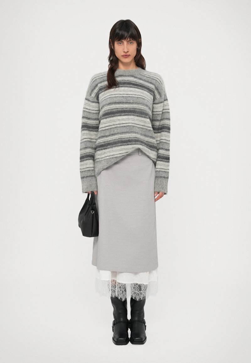 Sivi prugasti džemper širokog kroja, upareni sa sivom suknjom slojevitom preko bijele čipkaste obrube. Crne kožne čizme do koljena i crna torba.