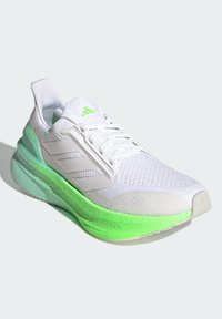 Weißer Sportschuh mit strukturiertem Obermaterial, grüner Außensohle und Akzenten. Verfügt über drei weiße Streifen an der Seite und eine gepolsterte Zunge.