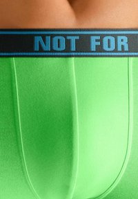Close-up of bright green boxer briefs with black waistband displaying blue text "NOT FOR".
