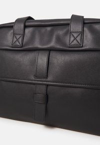 Bolso de cuero negro con una textura suave, dos asas resistentes y un diseño minimalista con acentos de costura horizontal y vertical.