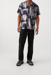 Lyhythihainen nappipaita, jossa on abstrakti kuvio tummansinisessä, vaaleansinisessä ja mauve-värissä. Yhdistetty mustiin cargo-housuihin ja harmaisiin lenkkareihin.