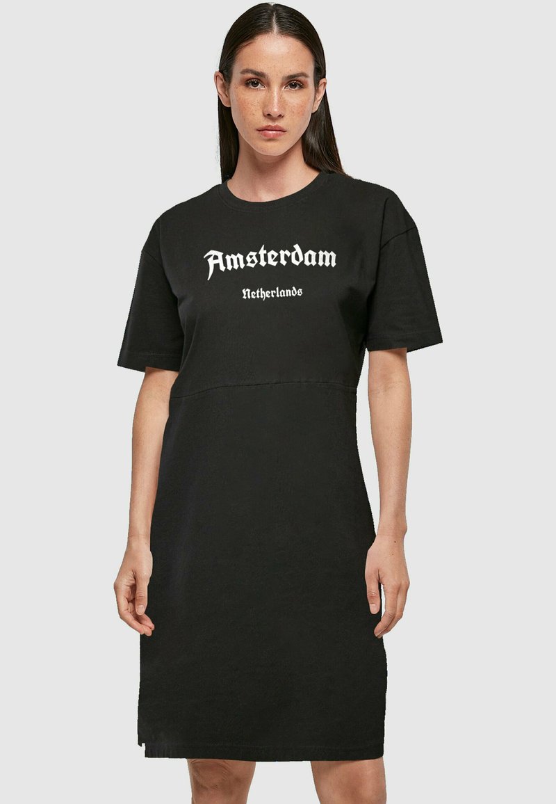 Čierna šaty s krátkymi rukávmi, s bielym potlačeným textom "Amsterdam Netherlands" na hrudi. Hladká látka, voľný strih.