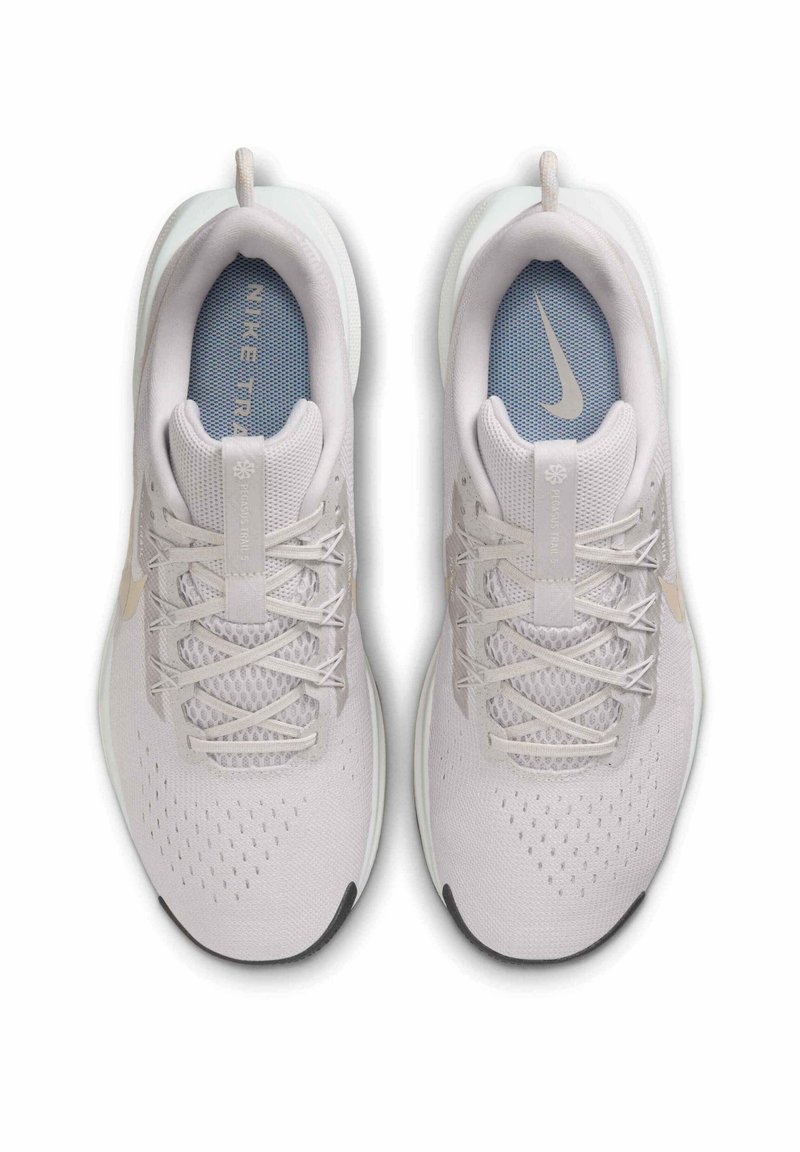 Zapatillas deportivas de color gris claro con parte superior de malla, puntera reforzada y suela blanca. Presentan cordones planos y acentos texturizados en la parte superior.