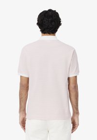 Polo shirt di un rosa chiaro con righe orizzontali, maniche corte e un colletto bianco, caratterizzato da un materiale texturizzato e un orlo dritto.