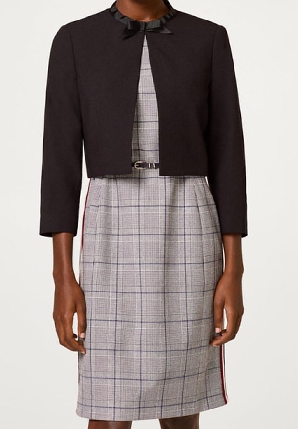 Veste courte noire avec un col en satin, associée à une robe grise à carreaux présentant une silhouette crayon et des bandes latérales rouges et bleu marine.