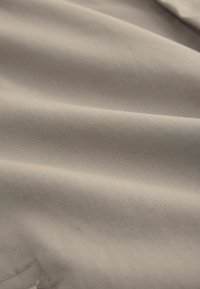 Gładka beżowa tkanina o subtelnym skośnym splocie i miękkich fałdach tworzących delikatne cienie i refleksy na powierzchni.