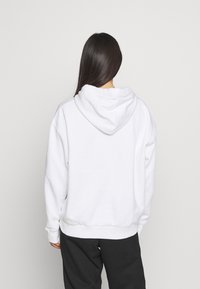 Witte katoenen hoodie met een ruime capuchon en geribbelde manchetten. Heeft een relaxed fit en een minimalistisch ontwerp, gezien vanaf de achterkant.