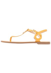 Gule flade sandaler med T-rem design, cirkulær detalje, justerbar ankelrem og tekstureret sål. Fremstillet af syntetisk materiale.