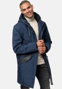 Parka acolchada azul marino con capucha, cierre de cremallera y un bolsillo frontal. Presenta un cuello forrado en forro polar y acentos en negro contrastantes.