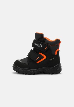 Botte d'hiver pour enfant noire et orange avec deux sangles Velcro et semelle robuste, étiquetée « superfit » et « GORE-TEX » pour l'imperméabilité.