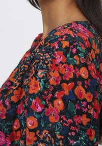 Blusa floral con un fondo negro y flores vibrantes en tonos naranja, rosa y verde. Tejido suave con un corte relajado y escote redondeado.