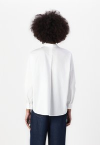 White button-up shirt with long sleeves, classic collar, and a vent at the back. Paired with dark blue denim trousers.