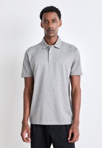 Pilkas polo marškinėliai iš minkštos medžiagos, turintys apykaklę, trijų mygtukų juostelę ir trumpas rankoves, dėvimi su juodomis kelnėmis.