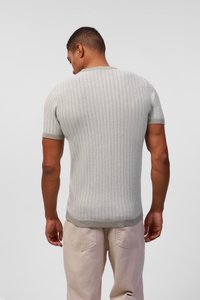 Hellgrauer kurzer Pullover mit strukturierter Musterung, kontrastierendem grünem Rippenkragen und -saum. Getragen von einer Person, die von hinten schaut.