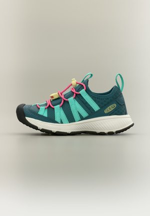 Udendørs sneaker i turkis og blågrøn med lyserøde elastiklisser, hvid sål, sort tåhætte og grønne træksløjfer, vist i siddeprofil.