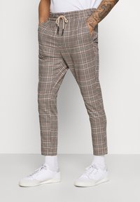 Geruite broek in neutrale kleuren met een elastische tailleband, aantrekkoord en zijzakken. Gecombineerd met witte sneakers en enkelsokken.