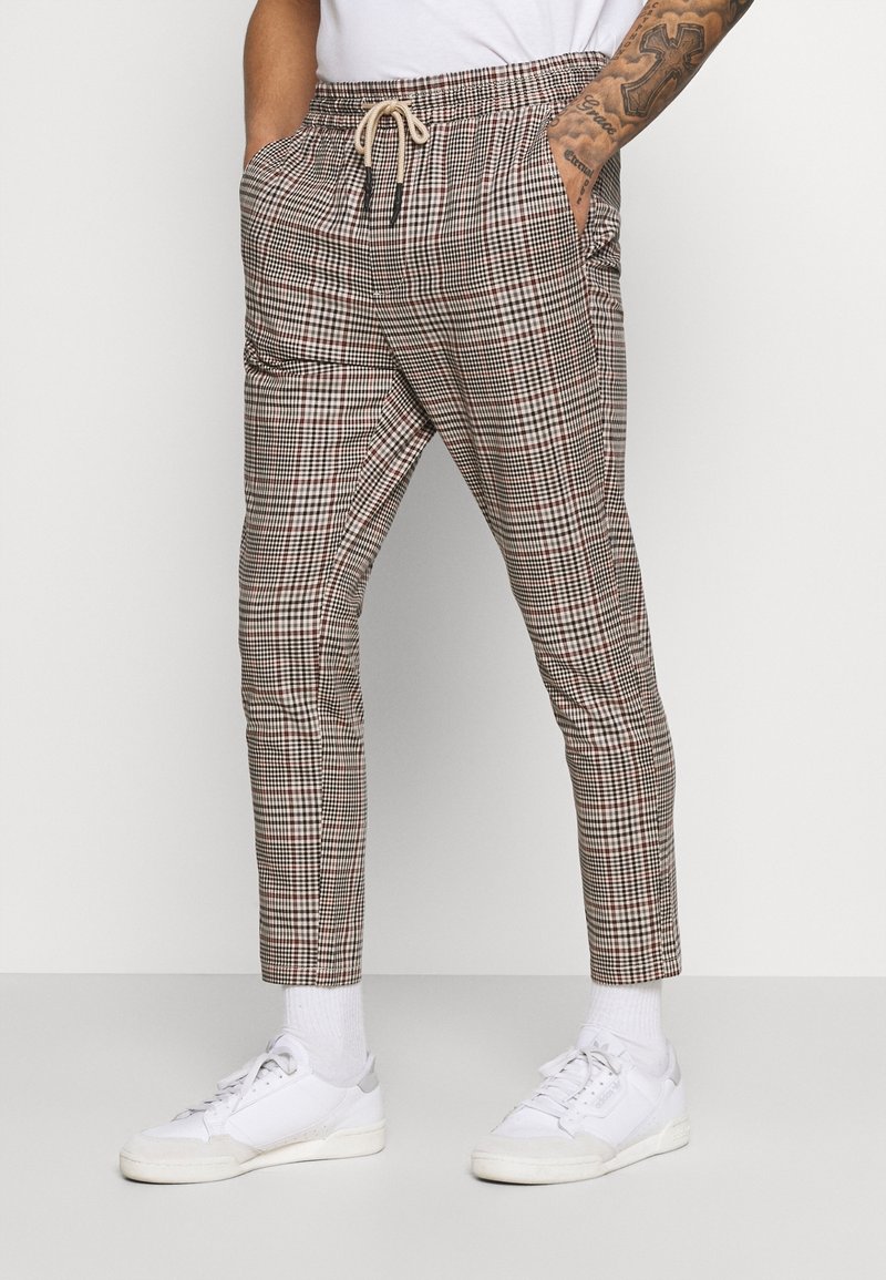 Geruite broek in neutrale kleuren met een elastische tailleband, aantrekkoord en zijzakken. Gecombineerd met witte sneakers en enkelsokken.