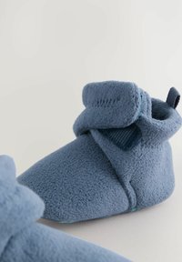 Niebieskie, miękkie kapcie z polaru o zaokrąglonym kształcie, z zagiętym mankietem i teksturowanymi akcentami. Posiadają design typu slip-on oraz minimalistyczne wykończenie.