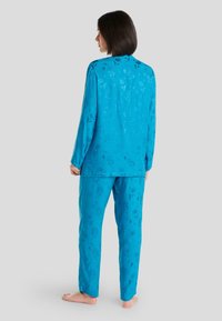 Conjunto de pijama azul que incluye una camiseta de manga larga y pantalones a juego con un estampado floral. La tela tiene una textura suave y lisa.