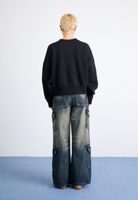 Svart oversize sweatshirt med rundad halsringning, i kombination med ljusblå vida cargojans med sidofickor och urtvättade detaljer.