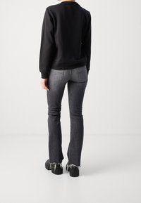 Sudadera negra, ajustada con mangas largas. Combinada con jeans acampanados gris oscuro con dobladillos deshilachados y bolsillos traseros. Zapatos de plataforma negros.