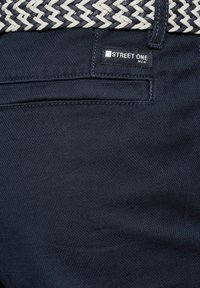 Donkerblauwe broek met een gestructureerde stof en een geweven riem in zwart en wit. Een "STREET ONE" label is zichtbaar op de tailleband.