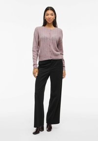 Svetlo mauve rebrast cardigan z okroglim izrezom, sprednjimi gumbi in dolgimi rokavi, združen z črnimi širokimi hlačami in temnimi gležnjarji.