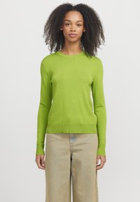 Maglione verde a maniche lunghe con scollo rotondo, polsini e orlo a costine. Abbinato a jeans a gamba larga chiari.