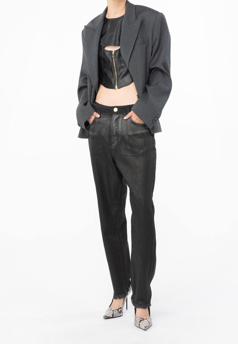 Top de cuero negro cropped con cremallera frontal, combinado con pantalones negros de corte holgado y una chaqueta gris estructurada. Tacones de piel de serpiente completan el look.