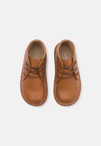 Zapatos de cuero marrón con puntas redondeadas, diseño de cordones y costura blanca contrastante, presentando un pequeño detalle bordado en el costado.