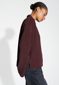 Bordeaux pullover gemaakt van textuurstof met een kraag, zijsplitten en een relaxte pasvorm, gecombineerd met donkere jeans.