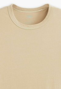 Camiseta beige con cuello redondo, hecha de una tela suave. El escote presenta una costura de contraste para mayor detalle. Textura lisa y diseño simple.