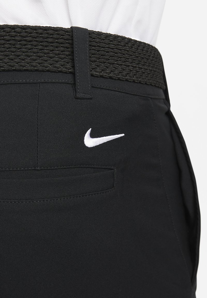 Sorte bukser lavet af glat stof med et tekstureret, sort vævet bælte. Har et hvidt Nike-logo på baglommen.