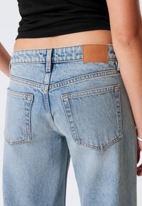 Ljust blå denimjeans med hög midja, med en beige läderetikett, rak passform och synliga sömmar på fickor och sömmar.