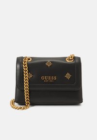 Sort læder crossover taske med en guldkæde-strop, der har et guldlogo og udsmykninger, samt en flaplukning med dekorative detaljer.