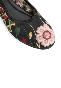 Chaussure plate noire avec broderie florale en rose, rouge et jaune sur une surface texturée, présentant un bout rond et un intérieur doux.