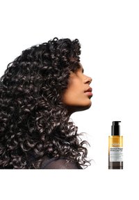 L'Oréal Professionnel Absolut Repair Molecular Oil i en pumpflaske ved siden av en profilvisning av en person med tykt, mørkt, krøllete hår og et nettingoverdel.