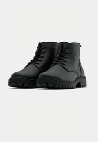 Black ankle boots made of smooth leather with a lace-up design, featuring a chunky tread sole and stitched detailing on the sides.