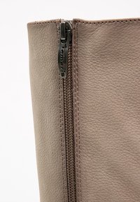 Bottine en cuir taupe avec fermeture éclair latérale, présentant des coutures distinctes et une finition texturée pour un détail supplémentaire.