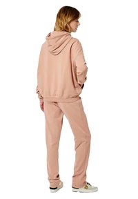 Sudadera rosa con capucha, con un corte relajado y puños de canalé, combinada con pantalones rosa a juego. Tejido suave, con detalles mínimos.