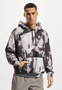 Črno-bela kapuca s tie-dye vzorcem, spredaj ima kenguru žep in napis "Club Life" odtisnjen čez prsi. Nastavljiva vrvica za pokrivalo.