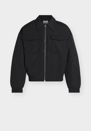 Veste noire zippée avec deux poches avant à rabat, col pointu, poignets et ourlet élastiques, présentée sur un fond blanc.