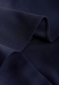 Tissu bleu marine foncé à surface lisse et légèrement texturée, plié pour montrer un tombé souple et une fine couture le long du bord.