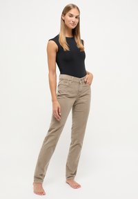 Beige, slim-fit, corduroy broeken met een platte voorkant, twee voorkantzakken en een klassiek vijf-pocket ontwerp. Gecombineerd met een zwart mouwloos bodysuit.